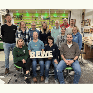 Führungskräfte-Team von REWE beim Teambuilding-Schreiner-Workshop mit den selbst gebauten REWE-Holzbuchstaben.