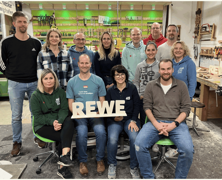 Rewe Teambuilding Führungskräfteworkshop Führungskräfte-Team von REWE beim Teambuilding-Schreiner-Workshop mit den selbst gebauten REWE-Holzbuchstaben.